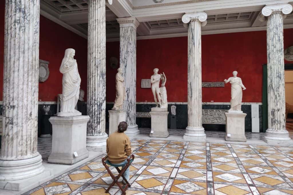 A woman sat in the Great Hall of the Glyptotek admiring the white plaster sculptures.